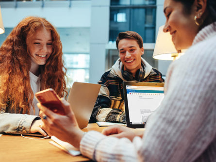 To elever sidder med deres bærbar og får demonstrereret noget på en mobil af en lærer